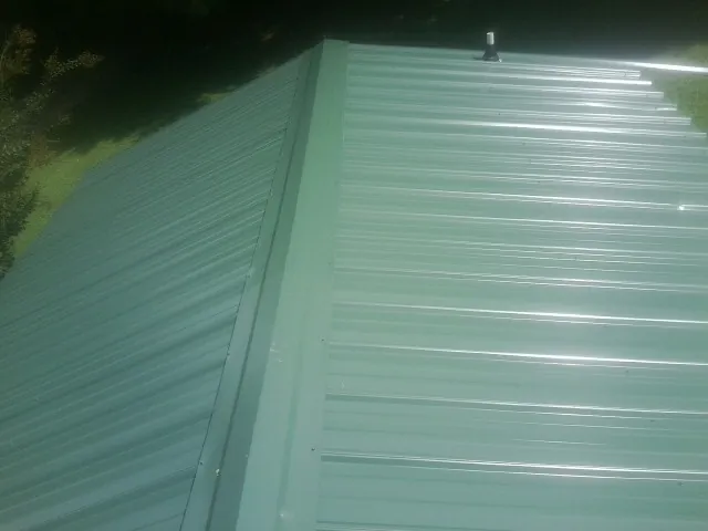 New green metal panels meeting at the ridge of a roof — Flat Roof Repair work by our crew in Dallas
