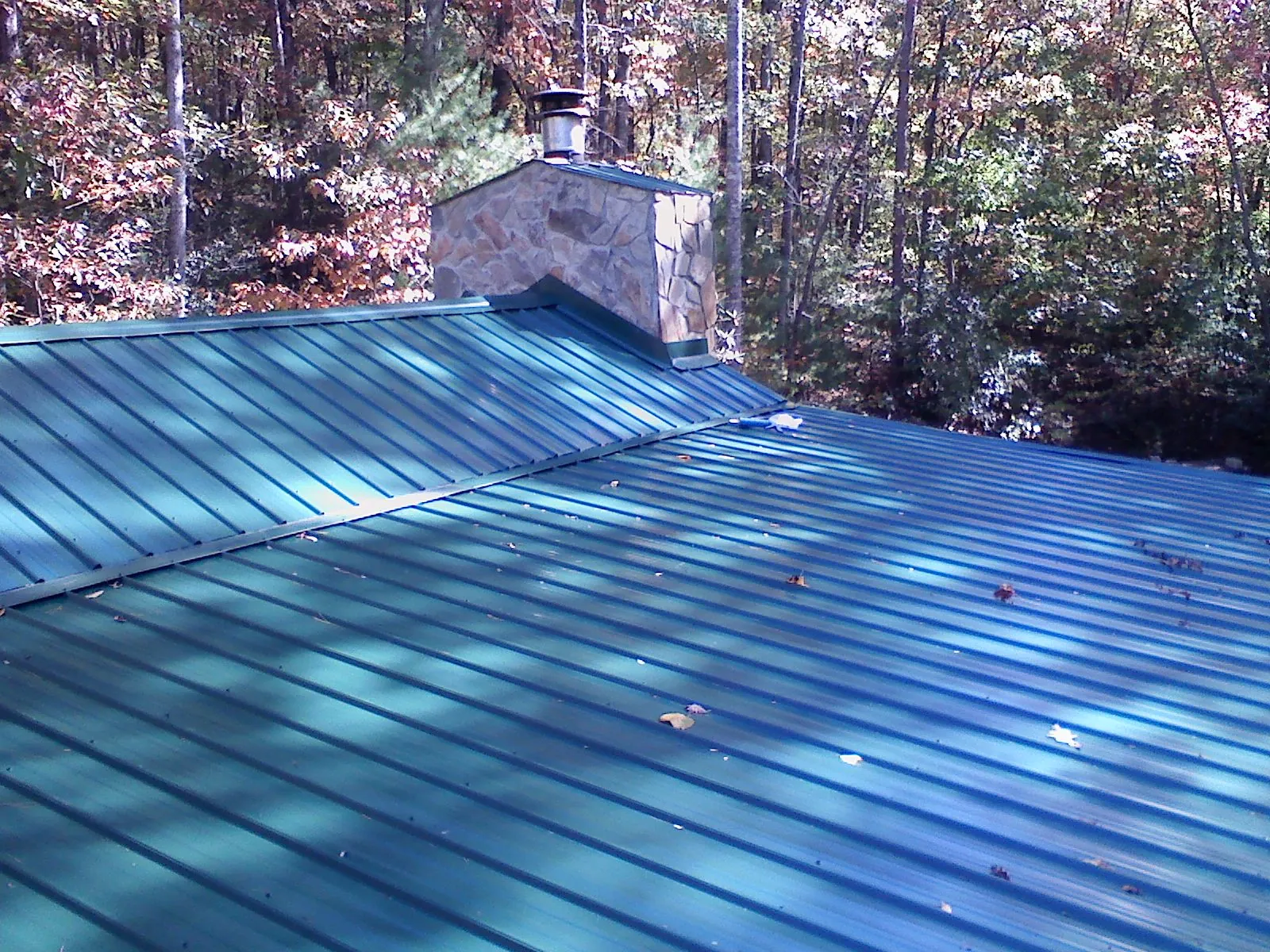 New green metal roof and stone chimney surrounded by autumn woods in Dallas