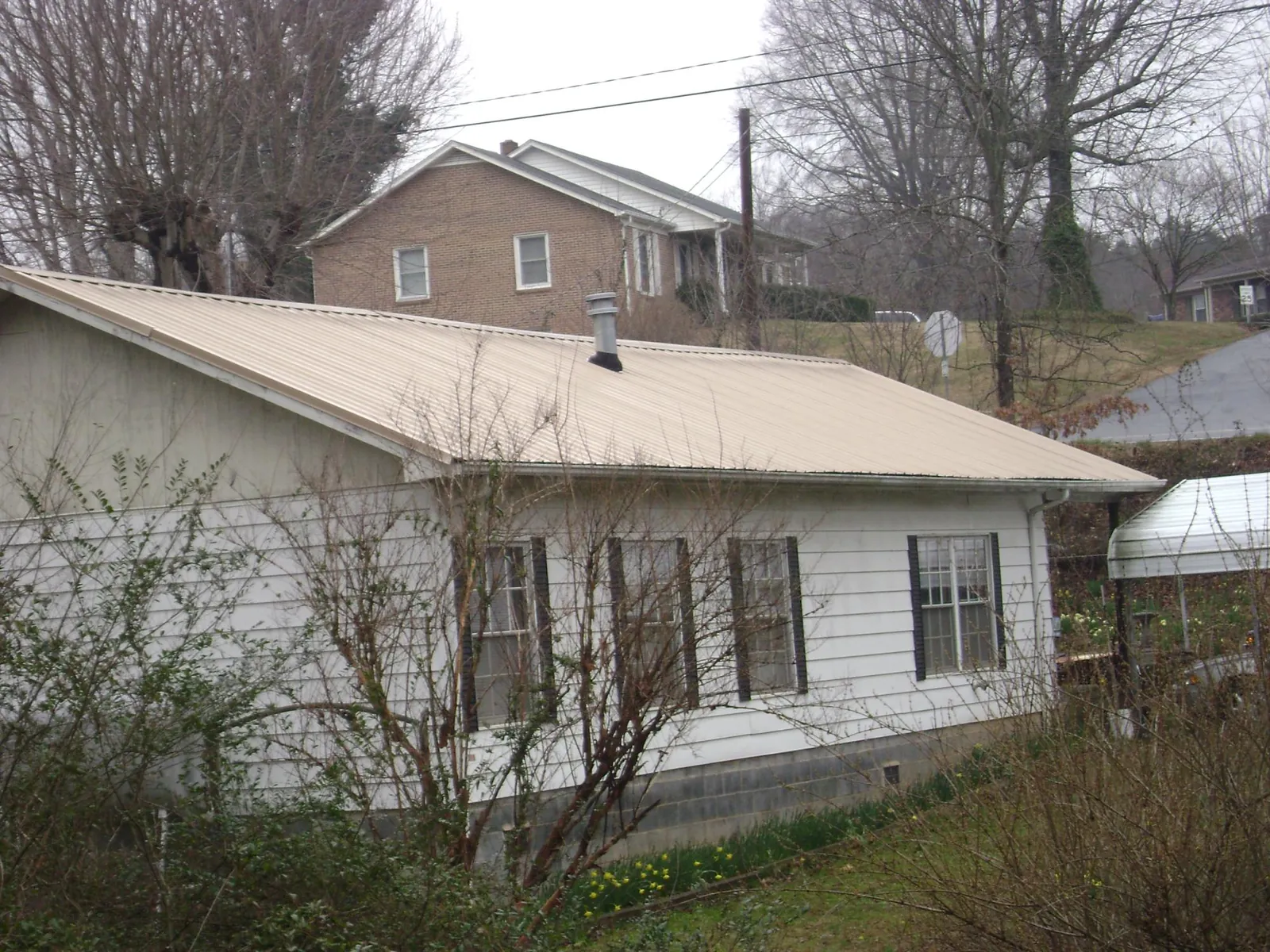 Tan metal roof on a white sided house set into a hillside — Commercial Roofing by Roofing Brothers in Dallas